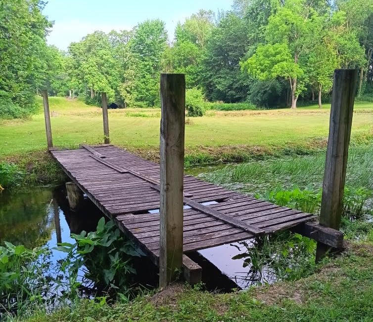 Old wooden bridge at Wolcott Park before replacement, with weathered, uneven planks crossing the creek